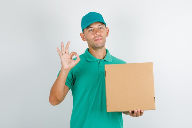Delivery man holding box and doing ok sign in green t-shirt and cap