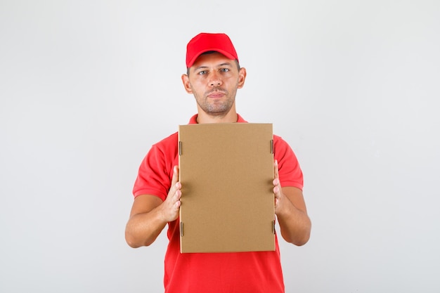 Экспедитор, держащий картонную коробку в красной форме. передний план.