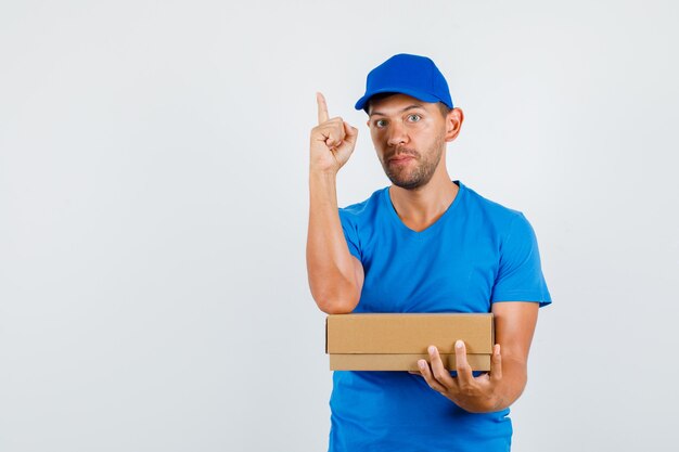 Delivery man holding cardboard box with finger up in blue t-shirt
