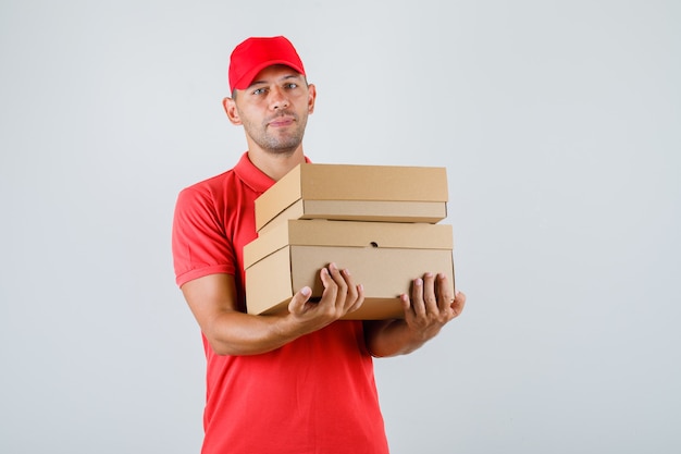 Delivery man holding cardboard boxes in red uniform , front view.