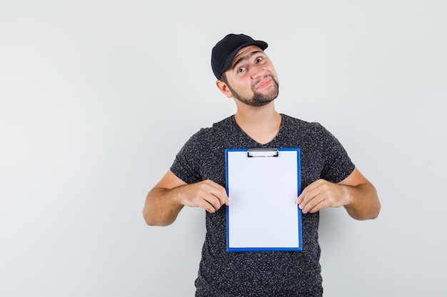 Delivery man holding clipboard in t-shirt and cap and looking positive