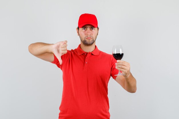 Delivery man holding glass of alcohol with thumb down in red t-shirt
