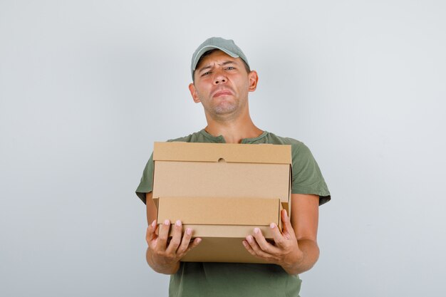 Delivery man holding heavy cardboard boxes in army green t-shirt, cap front view.