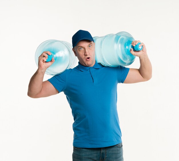 Доставка человек держит тяжелые бутылки с водой на плечах