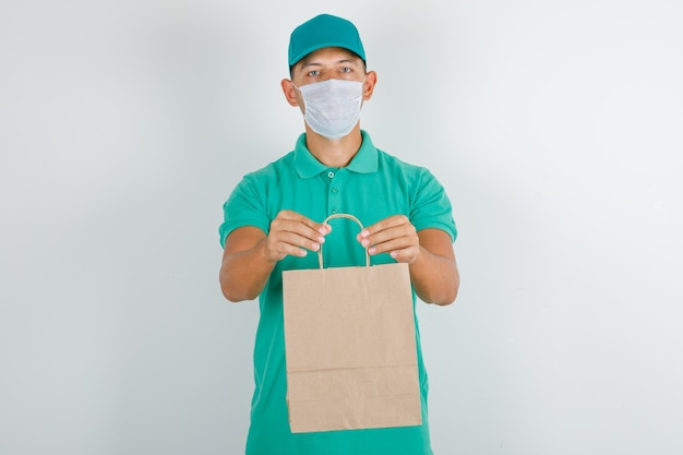 Free photo delivery man holding paper bag in green t-shirt with cap and mask