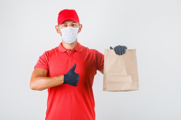 Delivery man holding paper bag and showing thumb up in red uniform