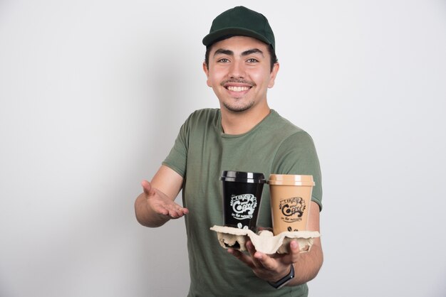 Delivery man holding takeaway cups of coffees on white background.