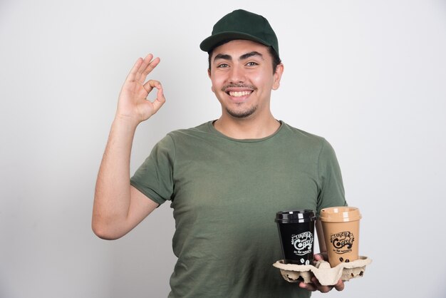 Delivery man holding takeaway cups of coffees on white background.