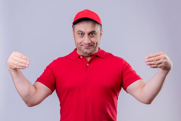 빨간 유니폼과 모자, 손으로 몸짓, 미소, 흰색에 서있는 신체 언어 개념에 배달 남자