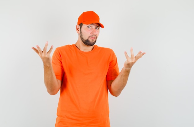 Бесплатное фото Доставщик в футболке, подняв руки кепки, показывая озадаченный жест, вид спереди.
