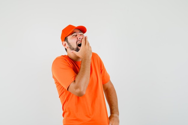 Delivery man laughing with hand on mouth in orange t-shirt, cap , front view.