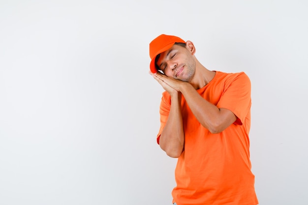 Delivery man leaning on palms as pillow in orange t-shirt and cap and looking peaceful