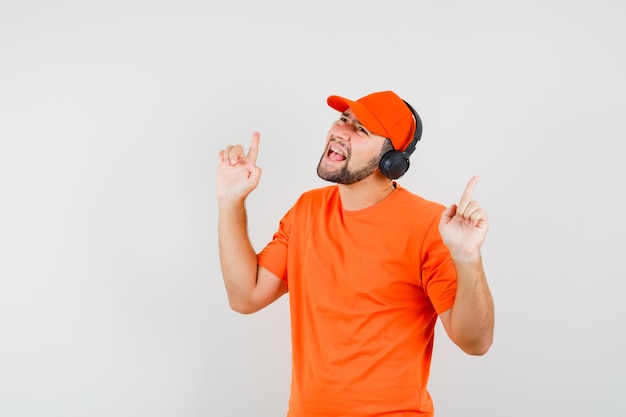 オレンジ色のTシャツ、キャップ、面白がってヘッドフォンで音楽を聴いている配達人。正面図。
