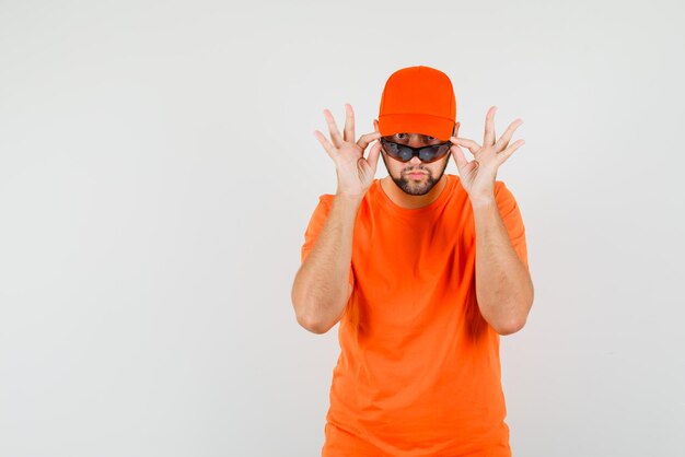 Доставка человек смотрит через очки в оранжевой футболке, кепке и выглядит сомнительно. передний план.