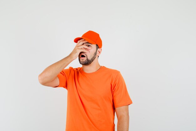 オレンジ色のTシャツ、キャップを指で見て、忘れて見える配達人、正面図。