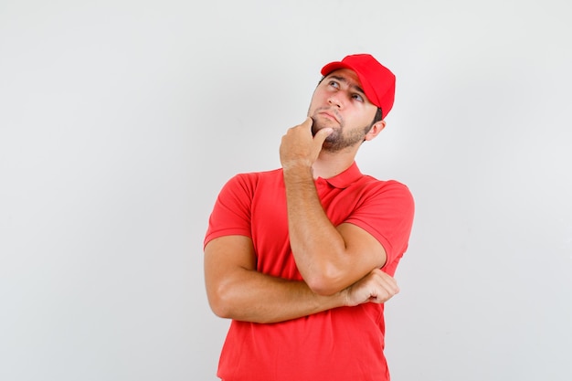 Uomo di consegna che osserva in su mentre tocca il mento in maglietta rossa