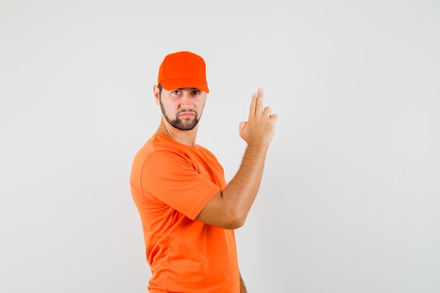 Il fattorino che fa il segno della pistola con il dito in maglietta arancione, berretto e sembra risoluto. vista frontale.