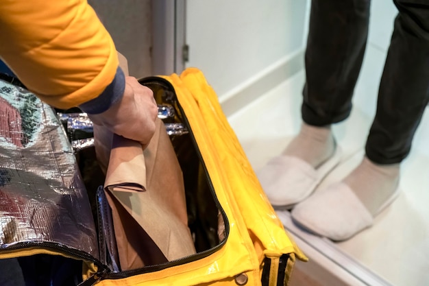配達人が黄色いバックパックを開けて、注文のあるバッグを持って、他の人の足