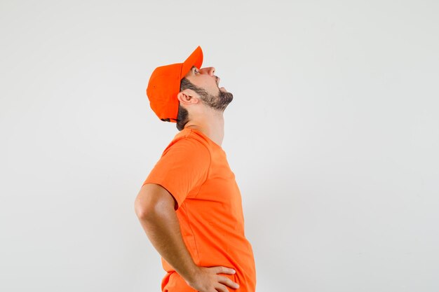 Delivery man in orange t-shirt, cap bending his head back and looking moody .