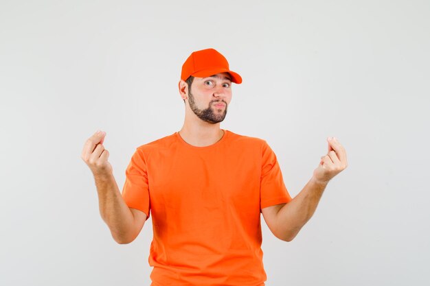 주황색 티셔츠를 입은 배달원, 두 손가락으로 몸짓을 하고 긍정적으로 보이는 모자.
