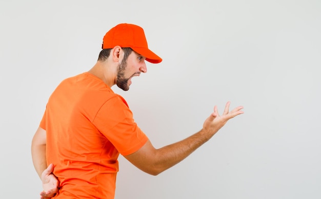 Delivery man in orange t-shirt, cap making asking question gesture and looking delirious .