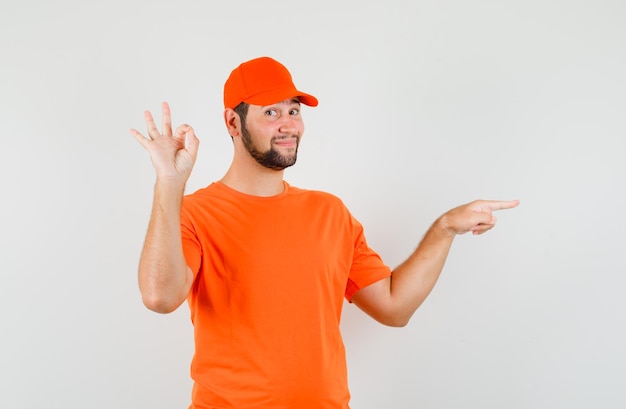 オレンジ色のTシャツを着た配達員、OKのサインが付いた側面を指し、陽気に見えるキャップ、正面図。