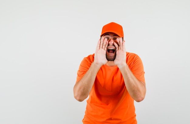 Доставщик в оранжевой футболке, кепке кричит или объявляет что-то, вид спереди.