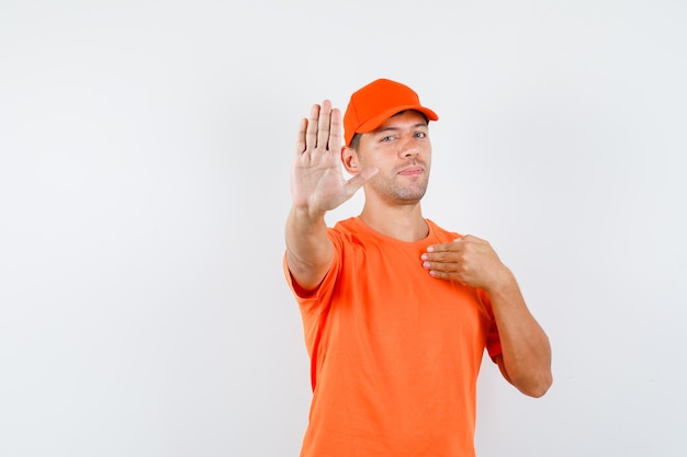 주황색 티셔츠와 모자에 배달 남자가 자신을 가리키고 자신감을 보임으로써 중지 제스처를 보여주는
