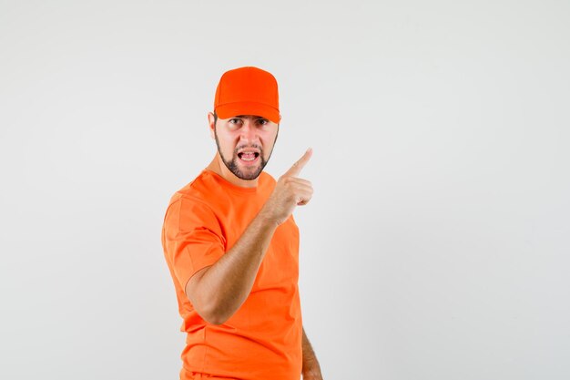 주황색 티셔츠를 입은 배달원, 손가락으로 모자를 경고하고 화난 표정을 짓고 있는 앞모습.