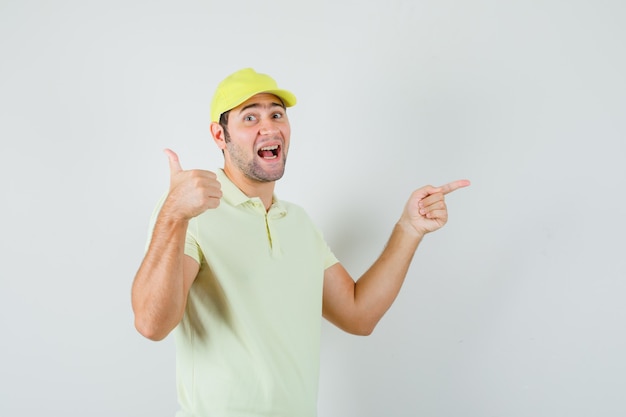 Delivery man pointing aside, showing thumb up in yellow uniform and looking happy , front view.