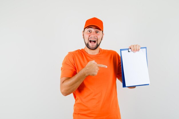 Delivery man pointing at clipboard in orange t-shirt, cap and looking optimistic , front view.