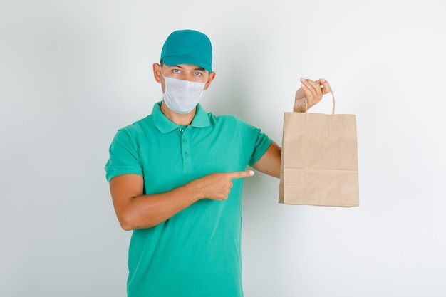 Delivery man pointing paper bag with finger in green t-shirt with cap