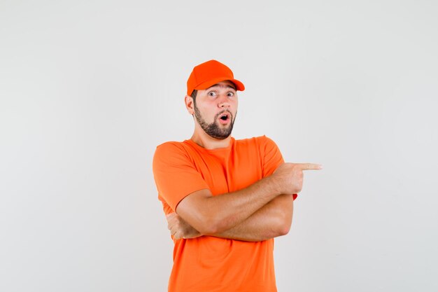 オレンジ色のTシャツ、キャップで横を指してびっくりした配達員。正面図。