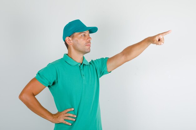 Delivery man pointing something with hand on waist in green t-shirt with cap