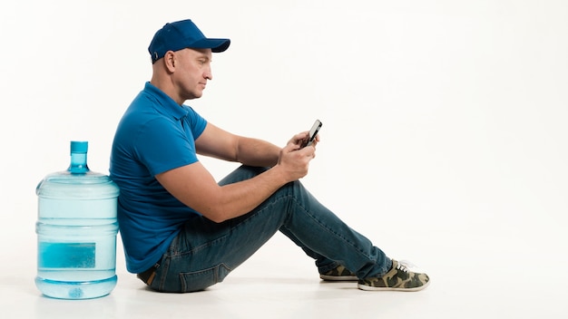 Free photo delivery man posing sideways while holding smartphone