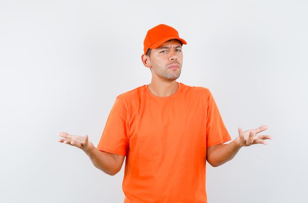 Delivery man raising hands in questioning manner in orange t-shirt and cap and looking confused