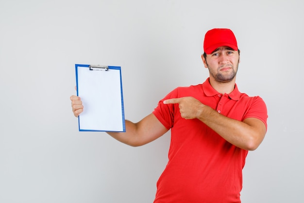Delivery man in red t-shirt, cap pointing at clipboard and looking bored