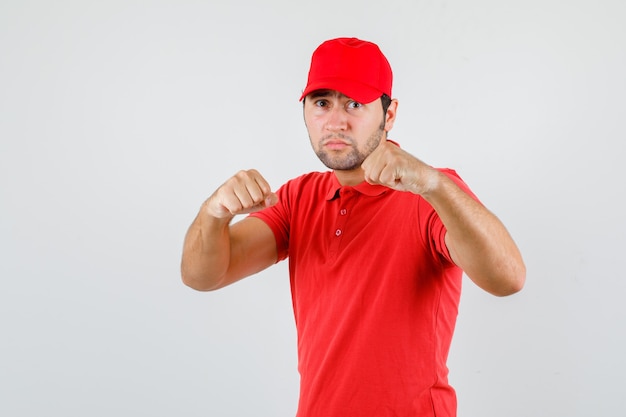 Delivery man in red t-shirt, cap standing in boxer pose and looking strong