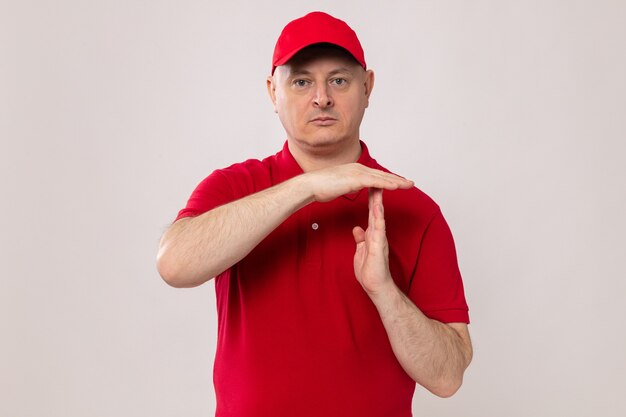 Доставщик в красной форме и кепке смотрит с серьезным лицом, делая тайм-аут руками