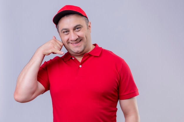 Free photo delivery man in red uniform and cap  smiling cheerfully making call me gesture standing