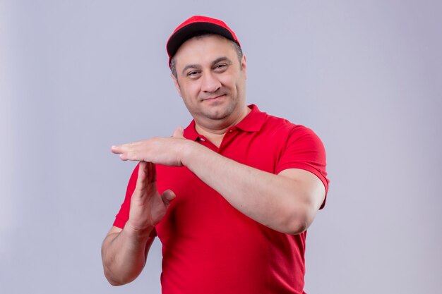 Delivery man in red uniform and cap smiling making time out gesture on white