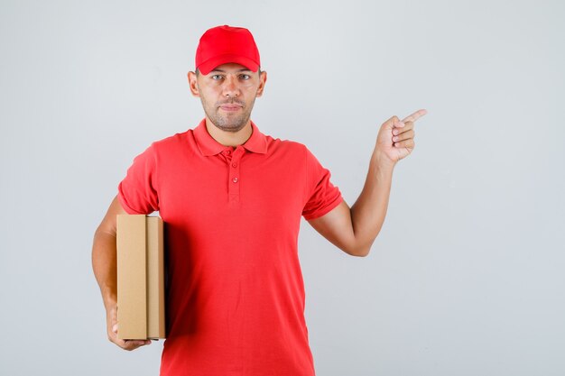 Доставщик в красной форме держит картонную коробку и указывает в сторону