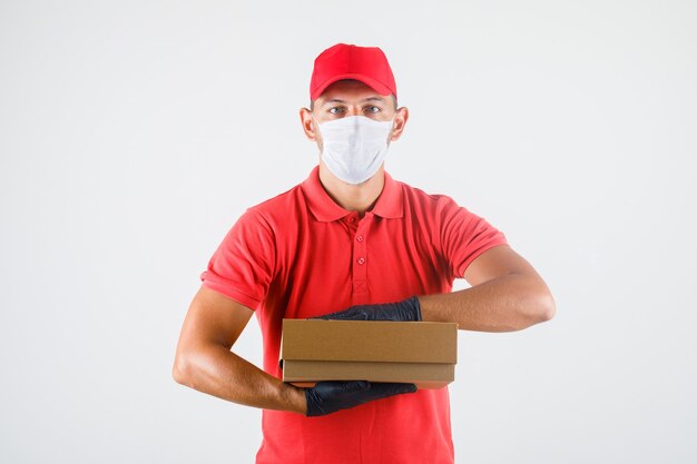 Курьер в красной форме, медицинская маска, перчатки, держащие картонную коробку