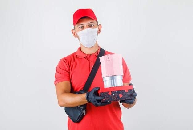 Delivery man in red uniform, medical mask, gloves holding present boxes