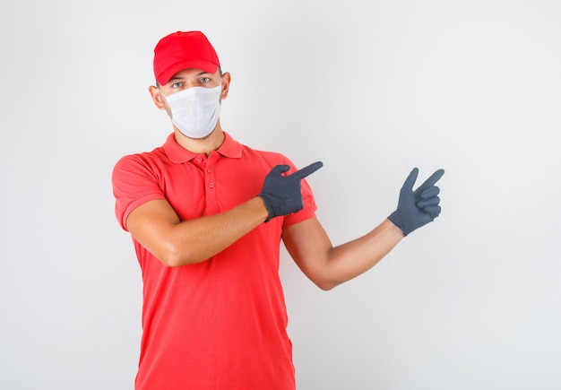 Free photo delivery man in red uniform, medical mask, gloves pointing fingers away and looking confident