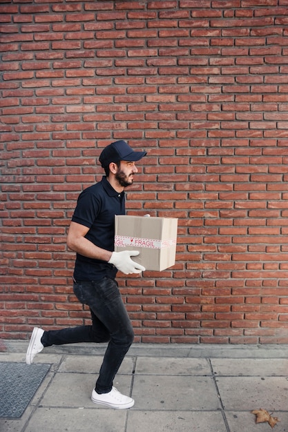 Delivery man running with parcel in front of brickwall