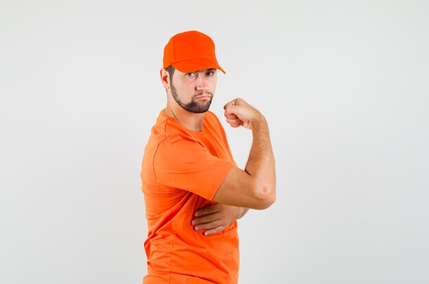 주황색 티셔츠, 모자를 쓰고 자신감을 갖고 있는 팔 근육을 보여주는 배달원.