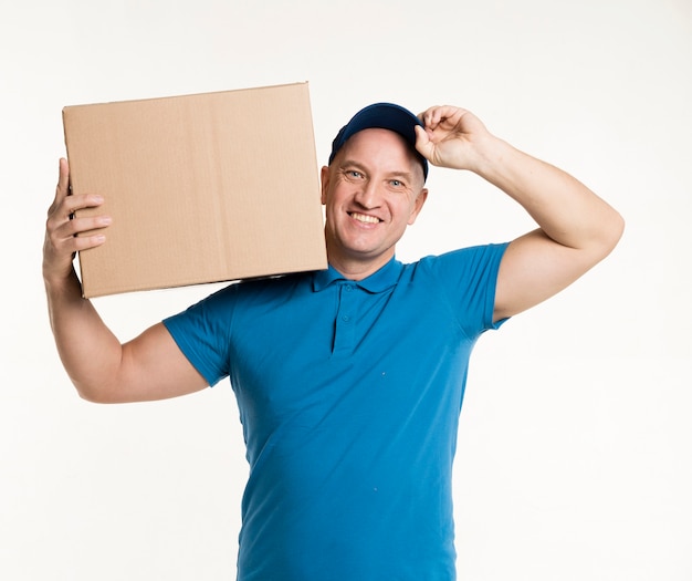 Delivery man smiling and posing with cardboard box on shoulder