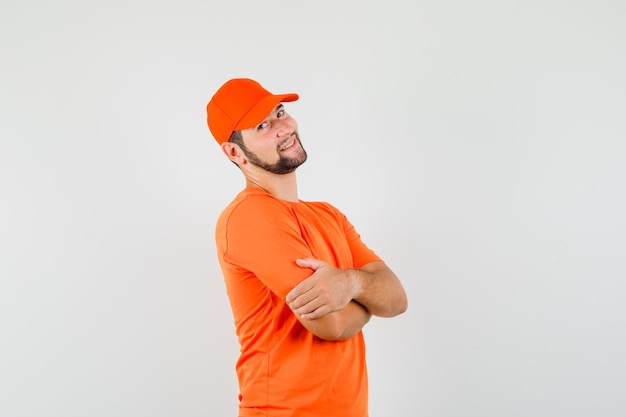 Доставщик, стоящий со скрещенными руками в оранжевой футболке, кепке и рад. передний план.