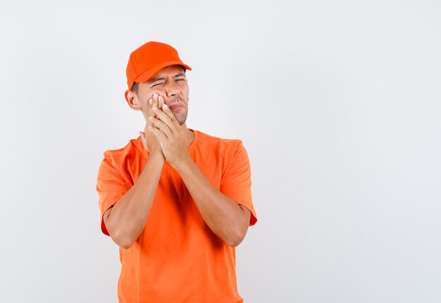 Delivery man suffering from toothache in orange t-shirt and cap and looking troubled